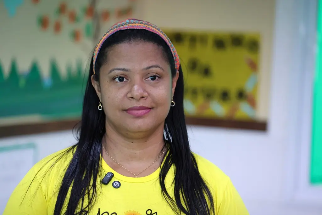 Foto horizontal em plano fechado que mostra a diretora da creche Nina Zaque, Katieannie Alves Silva. Ela é uma mulher negra, de cabelos pretos, longos e lisos, olhos pretos, usando tiara colorida e camiseta amarela.