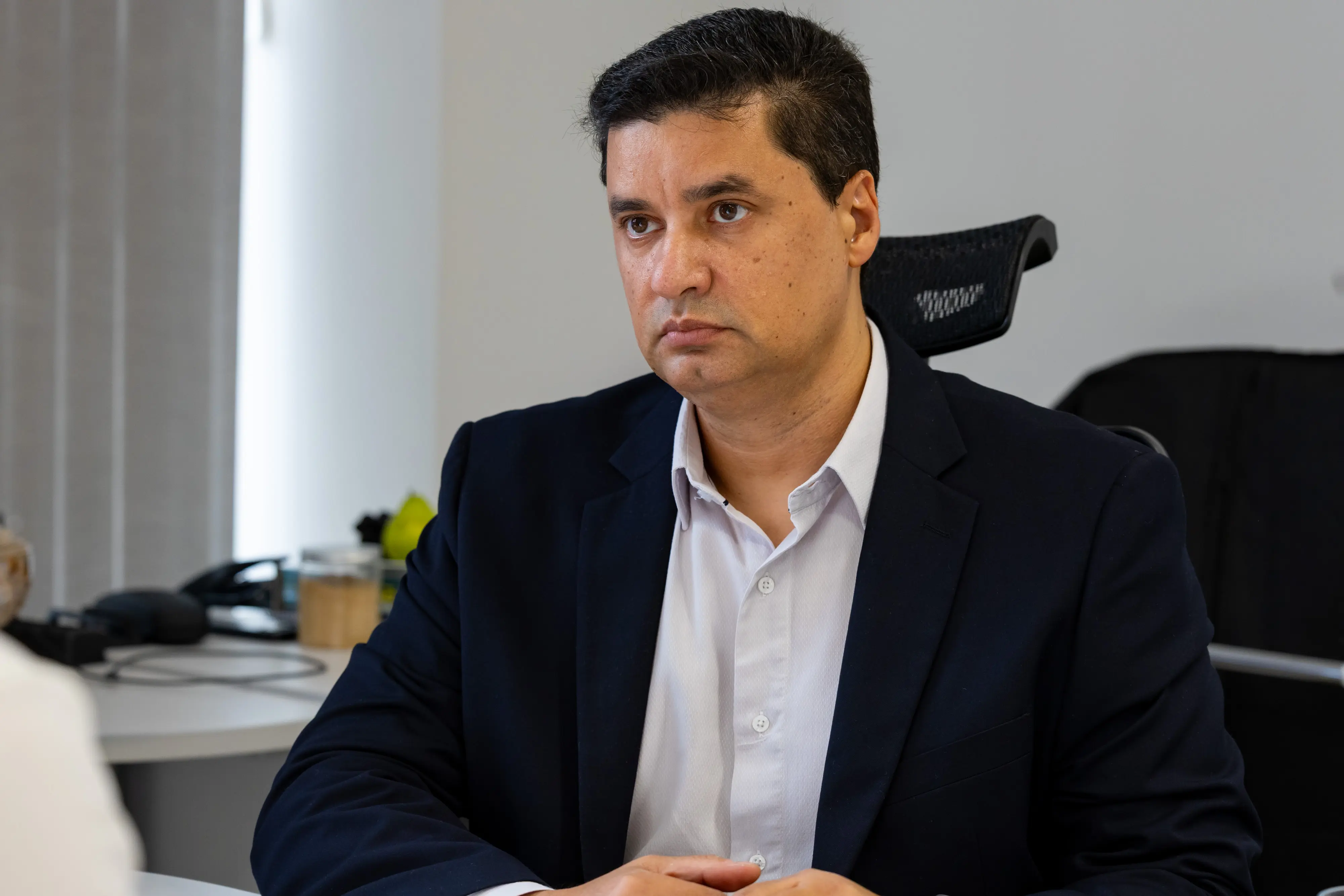 Retrato de um homem sentado em um escritório. Ele veste paletó escuro sobre camisa clara e olha atentamente para o lado.