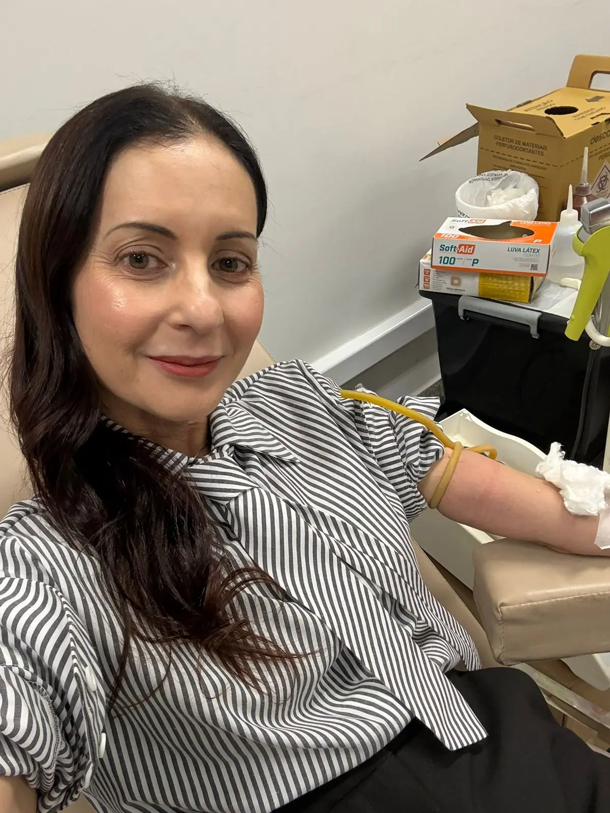 Mulher sorrindo em uma cadeira de coleta, com o braço esquerdo preparado para a doação de sangue.