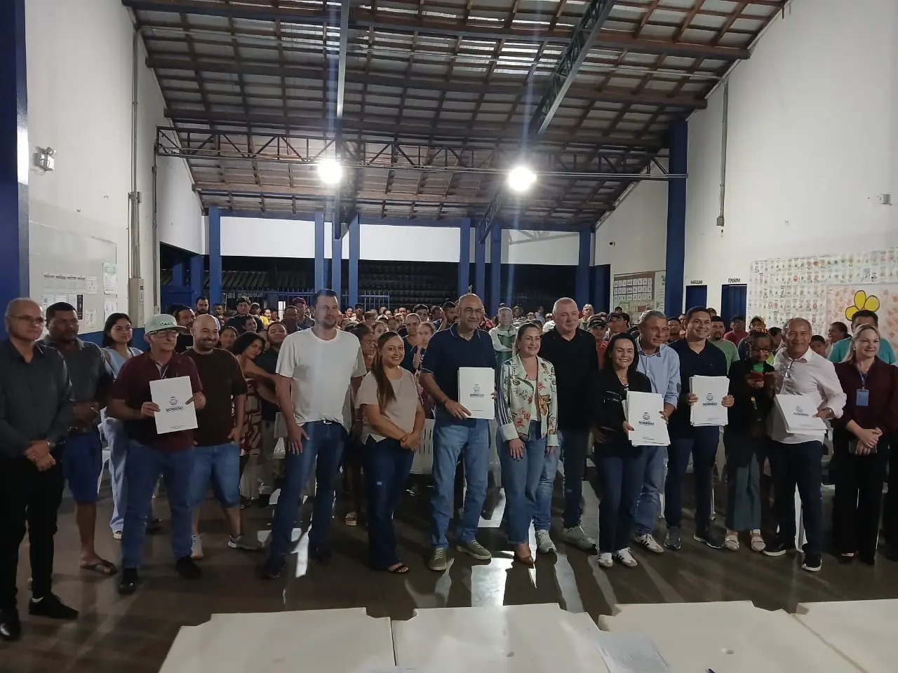 Moradores do bairro Boa Esperança II e autoridades posam para foto durante cerimônia de entrega de títulos definitivos de regularização fundiária realizada em Sorriso. Alguns dos participantes seguram os títulos em suas mãos.