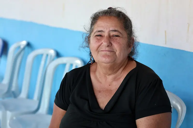 Foto horizontal colorida, em plano fechado, que mostra Sônia Maria Castelari sorrindo, sentada no corredor de uma escola onde ocorreu o mutirão Justiça em Ação. Ela é uma senhora parda, olhos castanhos, cabelos grisalhos e presos, usando camiseta preta. 