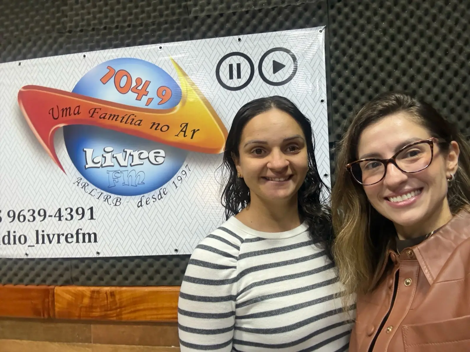 A imagem mostra a juíza da Vara Única da Comarca de Rio Branco, Luciana Sittinieri Leon, à esquerda, durante visita à Rádio Livre FM 104,9. Ao fundo painel da emissora, que exibe o nome da rádio e a frequência 104,9 FM.